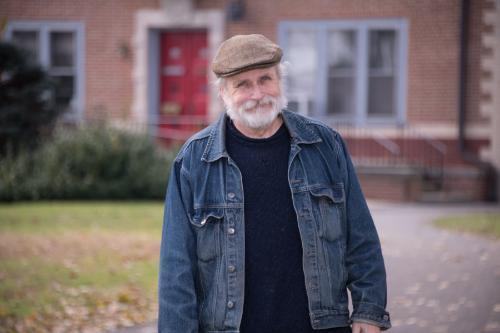 Man wearing beige hat and jean jacket posed in front of Gabriel House on Muhlenberg College campus.